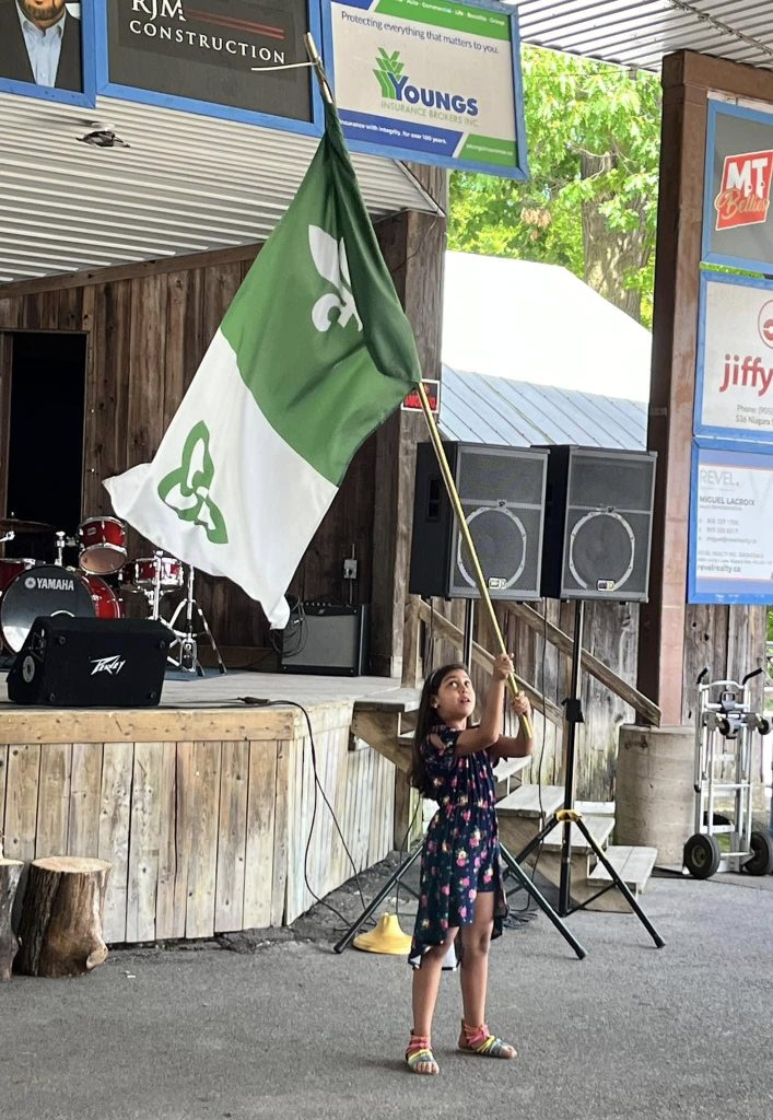 Jeune fille tenant le drapeau franco-ontarien lors de la fête de la Saint-Jean 2025. / Young girl holding the Franco-ontarien flag during the Saint-Jean celebration 2025.